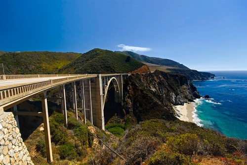 A scenic view of a coastal bridge spanning a cliffside, with lush greenery and the ocean in the background.