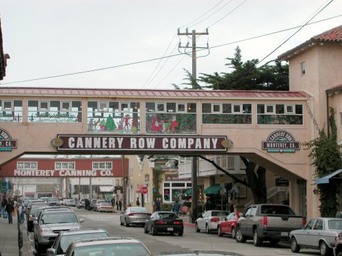 A view of Cannery Row Company with a pedestrian bridge and cars parked along the street in Monterey, California.