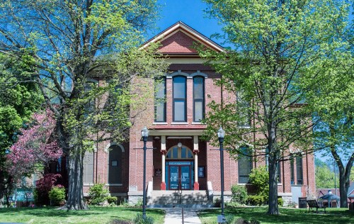 Historic brick building surrounded by trees and greenery under a clear blue sky.
