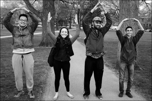 Four people standing on a path, forming the letters "O" and "H" with their arms, surrounded by trees.