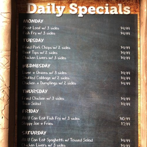 Chalkboard menu listing daily specials with prices, including meatloaf, pork chops, liver, and chicken dishes.