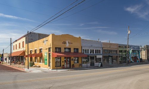A row of colorful storefronts along a quiet street under a clear blue sky.