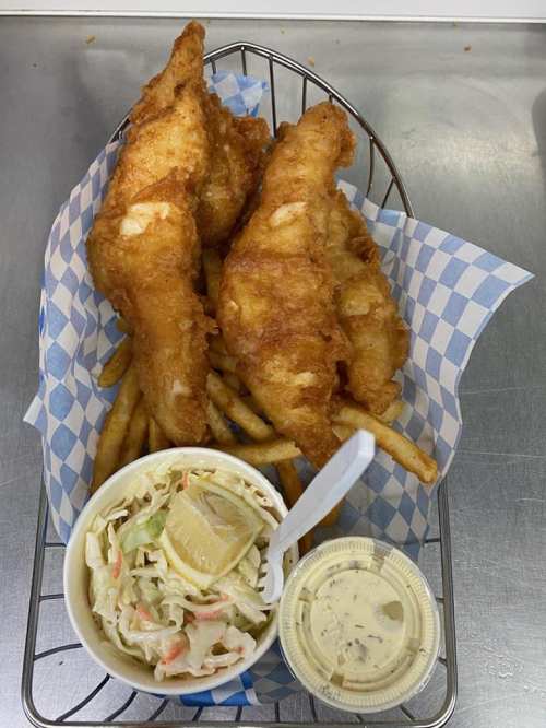 A basket of crispy fried fish fillets with French fries, accompanied by coleslaw and a small container of sauce.
