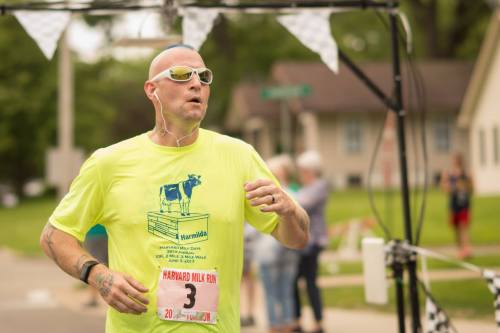 A man in a bright yellow shirt runs in a race, wearing sunglasses and earbuds, with a race bib number 3.