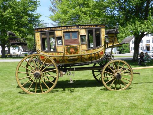 A vintage horse-drawn carriage with ornate decorations, parked on a grassy area surrounded by trees.