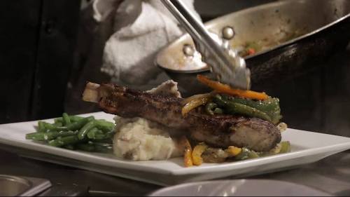 A plated dish featuring grilled meat with colorful peppers, served on mashed potatoes and green beans.