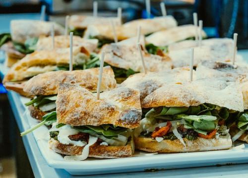 A platter of freshly made sandwiches with greens and sauces, each secured with a toothpick.