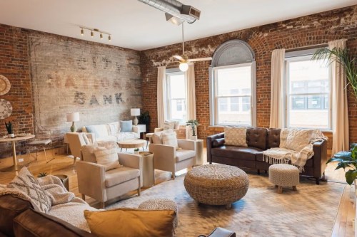Cozy living room with brick walls, large windows, comfortable seating, and a mix of modern and vintage decor.