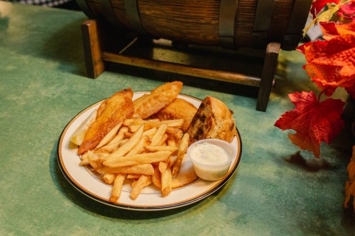 A plate of golden fries, crispy fish fillets, and a side of dipping sauce, set on a green table.