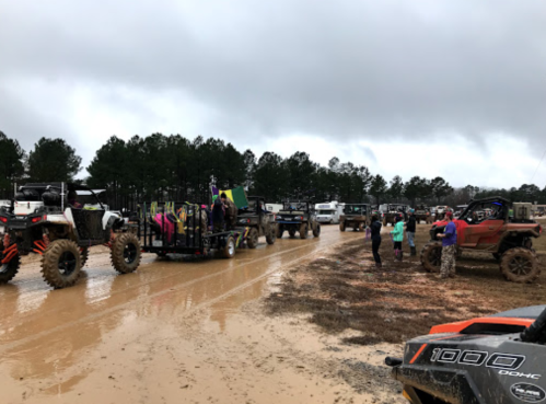 A muddy outdoor gathering with off-road vehicles and people socializing under cloudy skies.