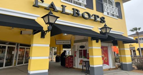 A storefront of Talbots featuring yellow walls, black awnings, and decorative lanterns.