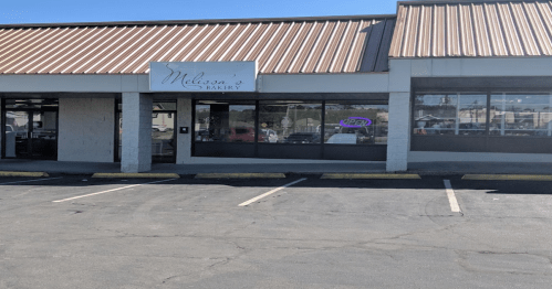 Exterior of Melissa's Bakery with a "Open" sign in the window and a parking lot in front.