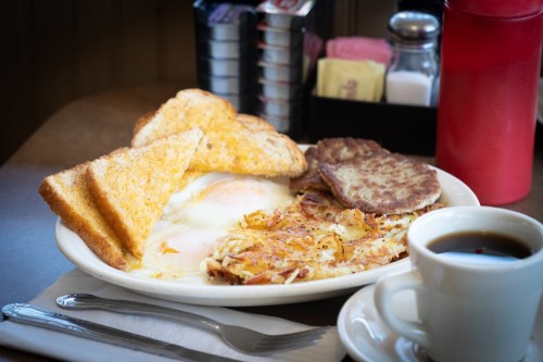 A plate of breakfast featuring eggs, hash browns, sausage patties, toast, and a cup of coffee on a table.