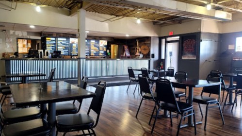 Interior of a casual dining restaurant with empty tables and a counter displaying the menu in the background.
