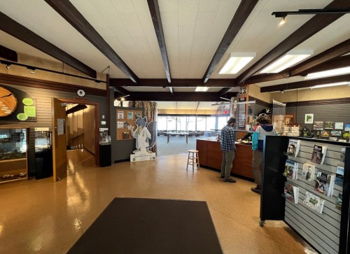 Interior of a visitor center with wooden beams, displays, and two people interacting at a service counter.