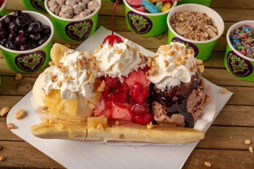 A colorful banana split topped with whipped cream, cherries, and nuts, surrounded by various ice cream toppings.