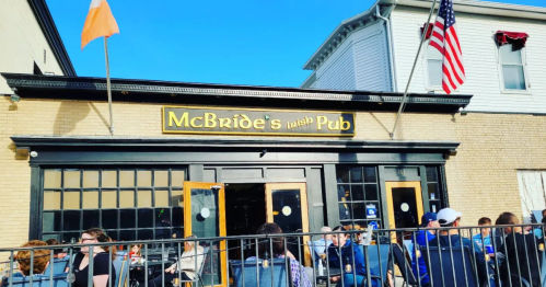Exterior of McBride's Irish Pub with outdoor seating, flags flying, and a clear blue sky in the background.