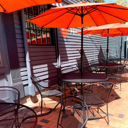 Outdoor café seating with black tables and chairs, shaded by bright orange umbrellas against a gray wall.