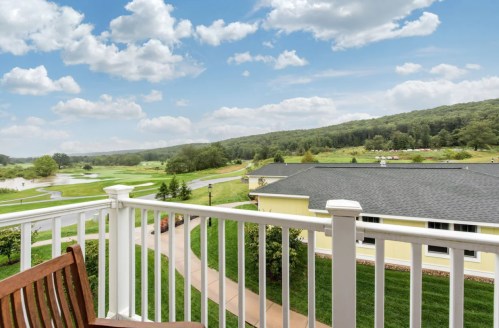A scenic view from a balcony overlooking green hills and a golf course under a partly cloudy sky.