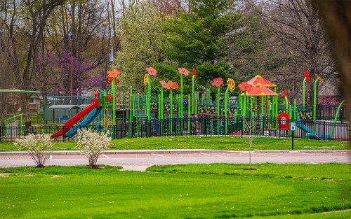 Colorful playground with flower-themed structures, slides, and greenery, set in a park with blooming trees.
