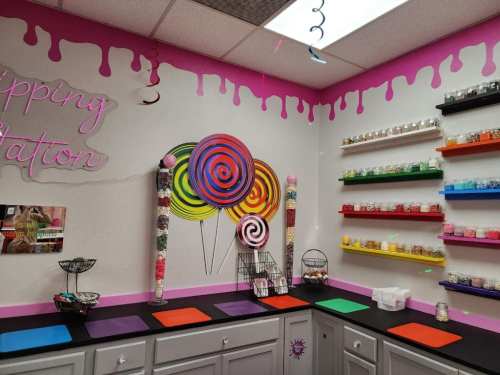 Colorful candy-themed room with a vibrant wall mural, shelves of toppings, and a black countertop for candy preparation.