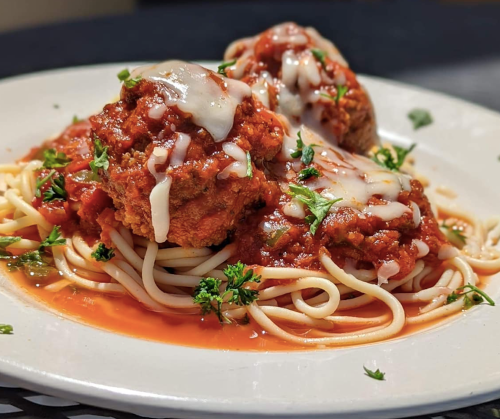 A plate of spaghetti topped with meatballs, marinara sauce, and melted cheese, garnished with parsley.
