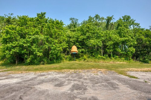 A large, cone-shaped structure stands in front of dense greenery, with a gravel area in the foreground.