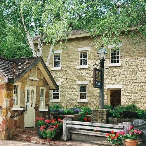 A charming stone building with a small entrance, surrounded by greenery and colorful flowers.
