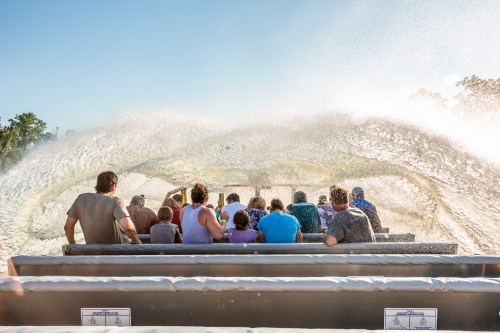 A group of people on a boat, splashed by water, enjoying a sunny day on a river or lake.