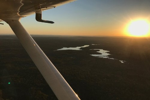 Aerial view of a sunset over a forested landscape with a winding river, seen from an airplane wing.