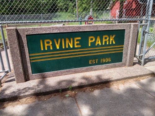Sign for Irvine Park, established in 1906, displayed on a stone structure near a fenced area.
