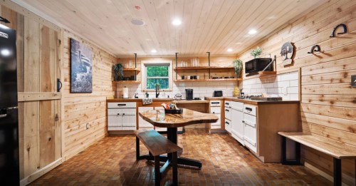 Cozy kitchen with wooden walls, a central table, and modern appliances, featuring a warm, rustic design.
