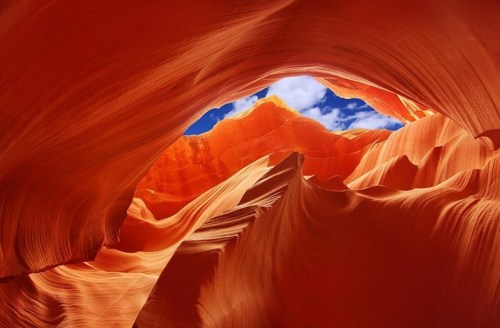 A stunning view of Antelope Canyon, showcasing vibrant orange rock formations and a bright blue sky above.