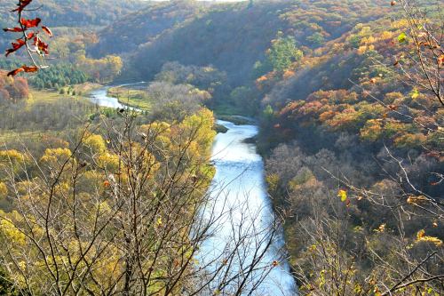 A winding river flows through a valley surrounded by colorful autumn foliage and bare trees.