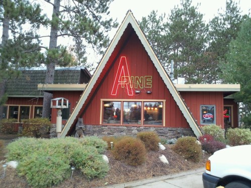 A-frame style restaurant with a red exterior, neon "OPEN" sign, surrounded by trees and shrubs.