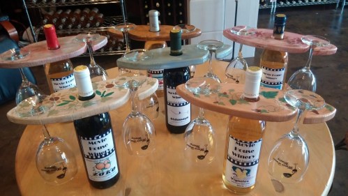 A display of wine bottles and glasses on wooden trays, arranged on a table in a wine shop.
