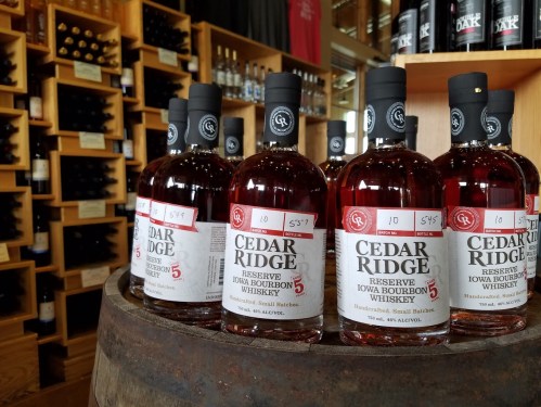 Bottles of Cedar Ridge Reserve Iowa Bourbon Whiskey displayed on a wooden barrel in a store.