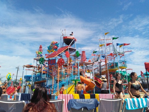 Colorful water park with slides and attractions, crowded with people enjoying a sunny day at the beach.