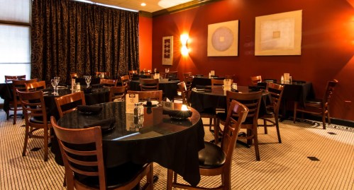 Elegant restaurant interior with dark wood tables, black tablecloths, and warm red walls, featuring abstract art.