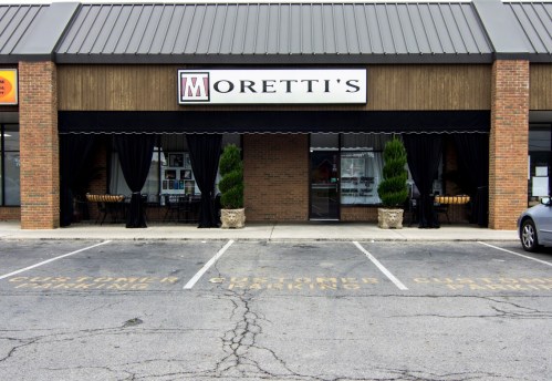 Exterior of Moretti's restaurant with a sign, large windows, and planters, featuring customer parking spaces in front.