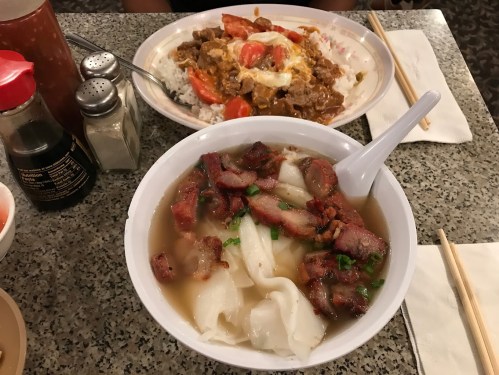 A bowl of noodles topped with sliced pork and green onions, alongside a plate of rice with meat and vegetables.