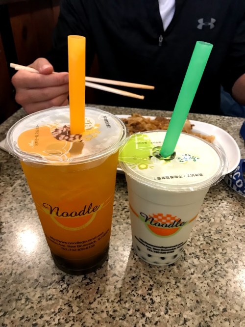 Two cups of bubble tea on a table, one with orange drink and the other with milk tea, both featuring colorful straws.