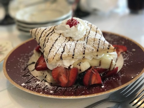 A delicious dessert featuring a layered crepe topped with whipped cream, strawberries, and a cherry on a plate.