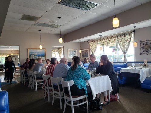 A group of people dining at a restaurant, seated at a long table with white tablecloths and blue booths in the background.