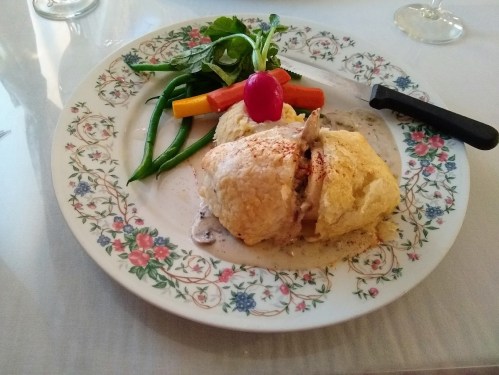 A plated dish featuring a baked chicken pastry, mixed vegetables, and a radish on a floral-patterned plate.