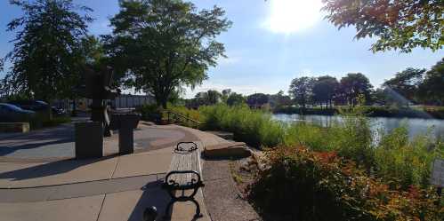 A serene park scene featuring a statue, a bench, and a river surrounded by greenery under a bright sky.