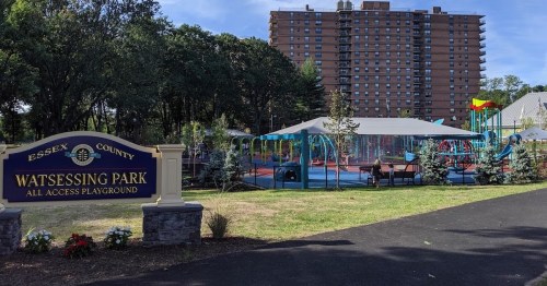 A playground at Watessing Park with colorful equipment, surrounded by trees and a sign indicating it's an all-access area.