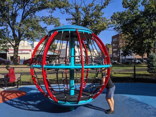 A colorful playground structure shaped like a globe, with a child playing inside and adults nearby on benches.