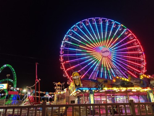 A vibrant carnival scene at night featuring a colorful Ferris wheel and illuminated rides.