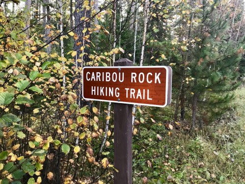 A wooden sign reading "Caribou Rock Hiking Trail" surrounded by trees and autumn foliage.